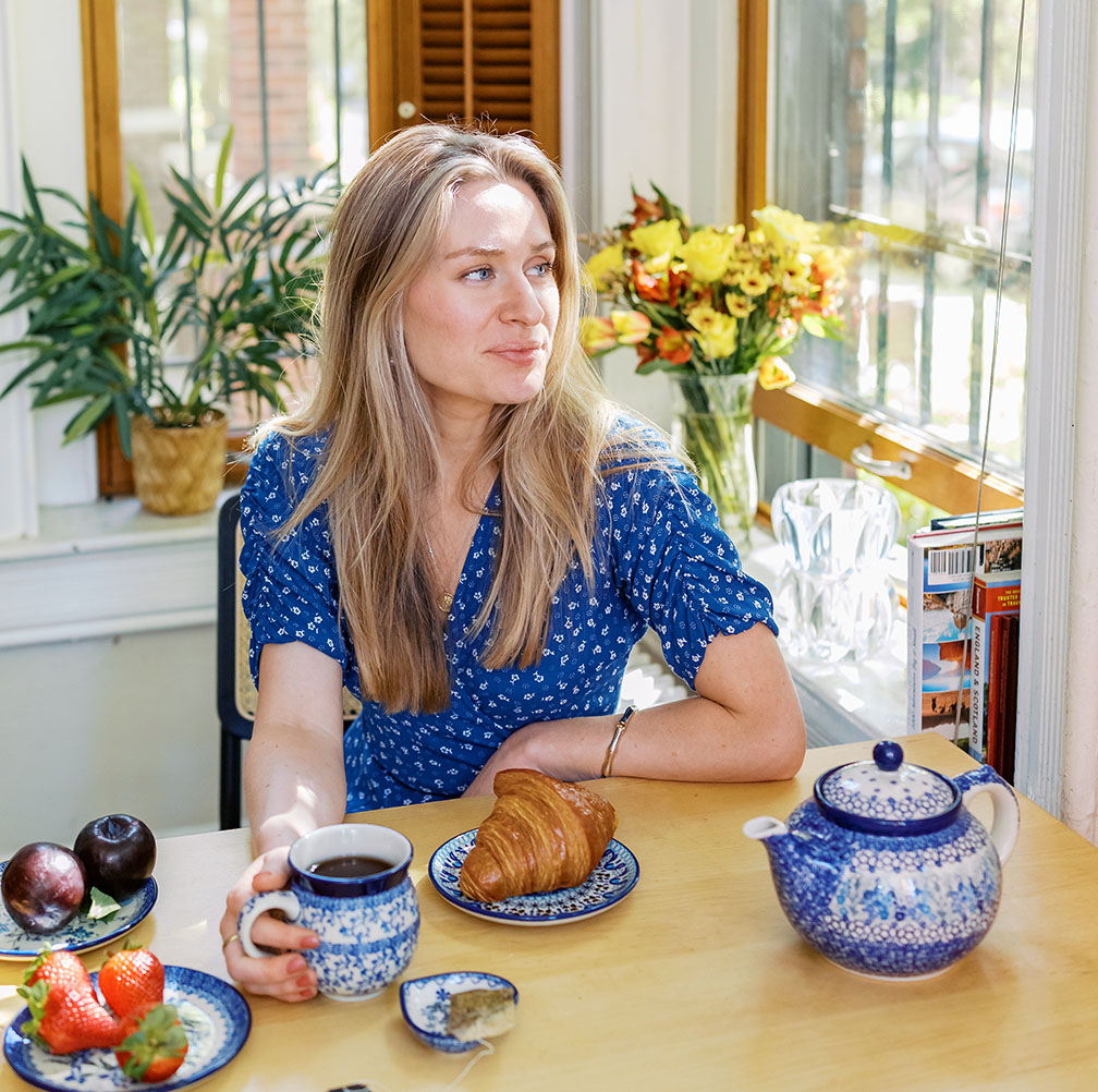 A woman enjoying a cup of coffee with a croissant, served on Bunzlau Castle tableware in a bright and cozy kitchen.