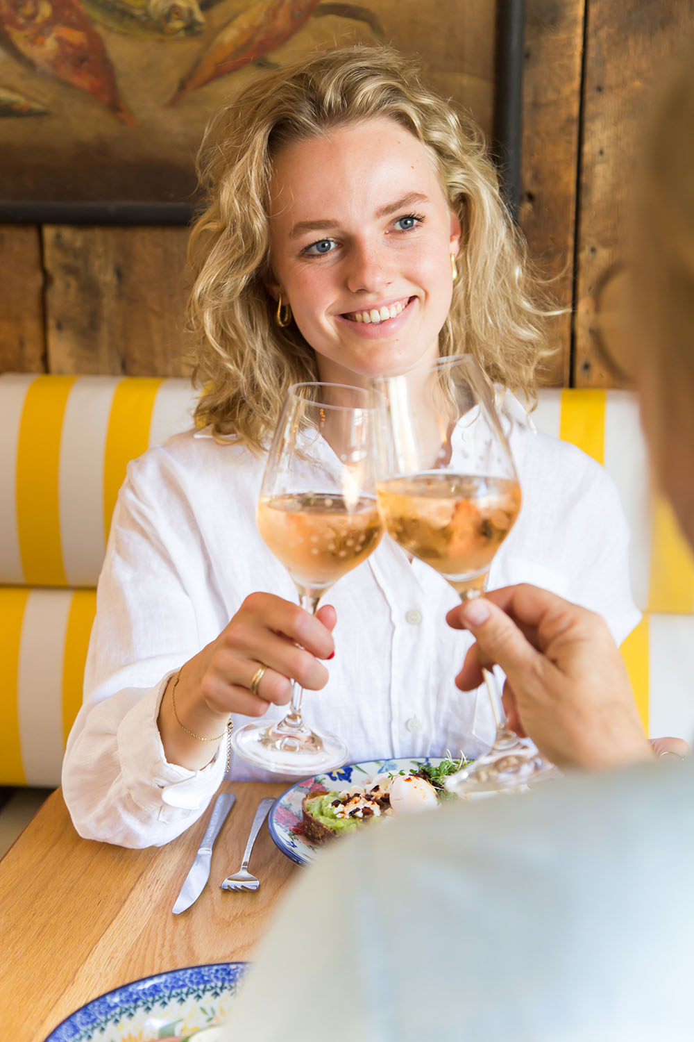 A woman raising a glass in a toast while dining with Bunzlau Castle tableware in a warm and inviting restaurant setting.