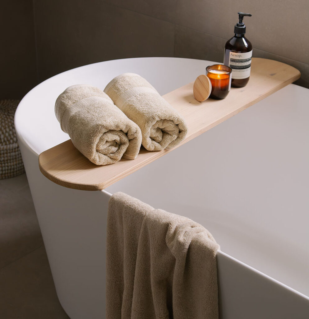 Rolled Organic Home cotton towels on a wooden bath tray beside a candle and soap, creating a calm and relaxing bathroom atmosphere.